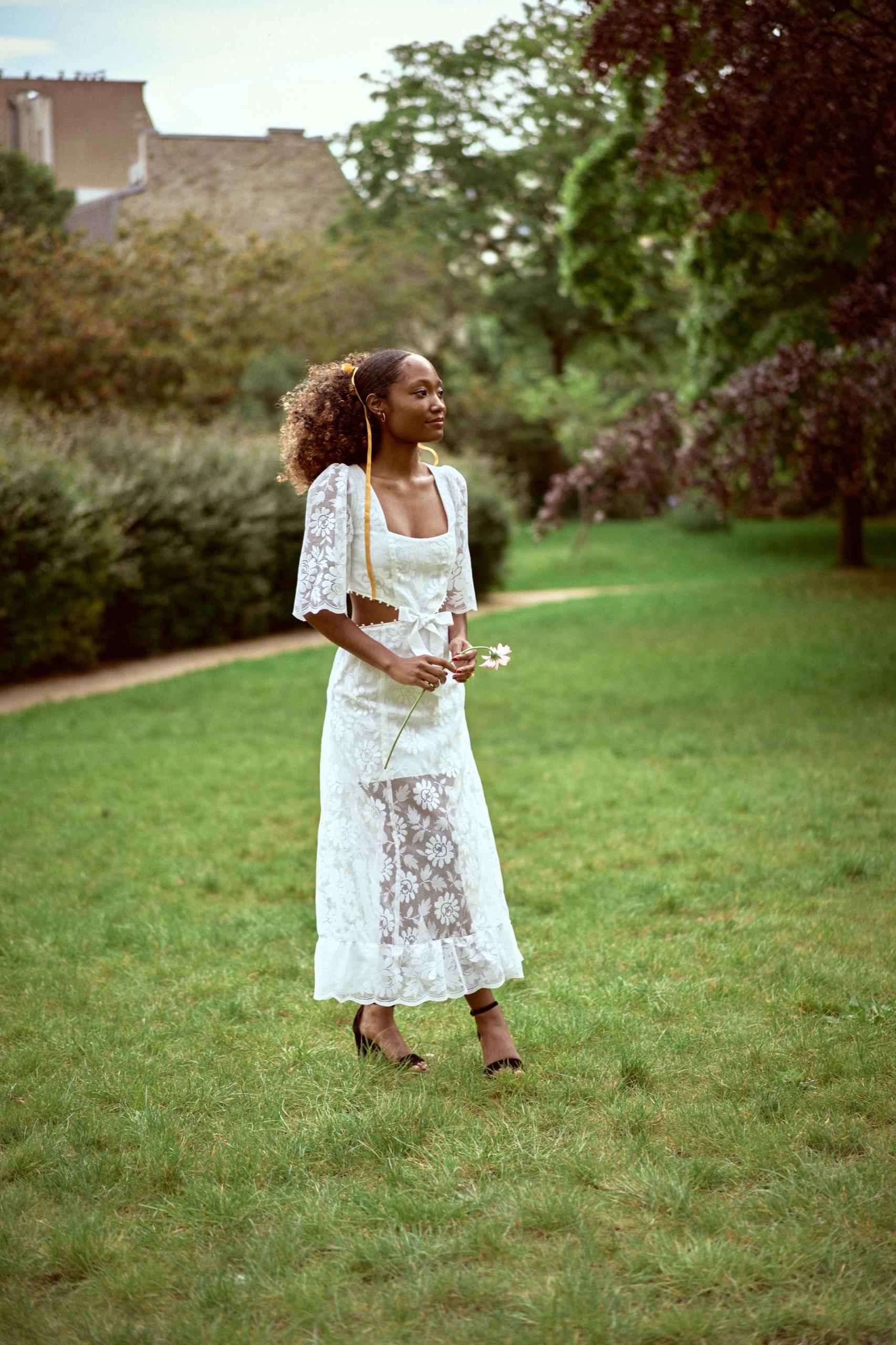 Une mariée en robe de dentelle dans un parc, une fleur à la main