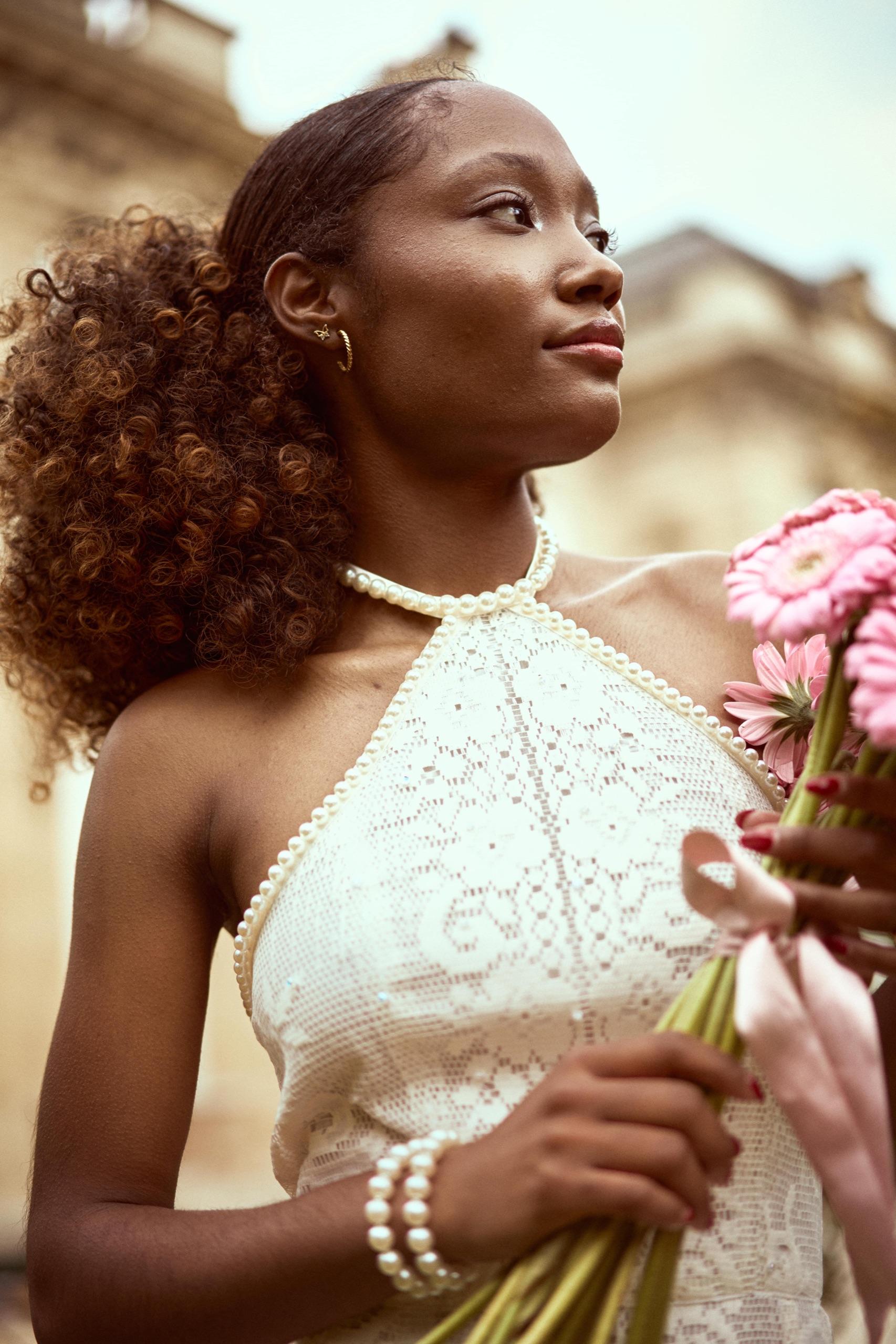 Une mariée en robe de dentelle et collier de perles, bouquet à la main